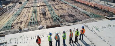 A row of construction workers on a concrete pad looking over a large area of prepped land