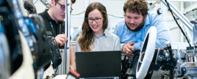 A team of 3 people looking at a computer inside an automobile testing facility